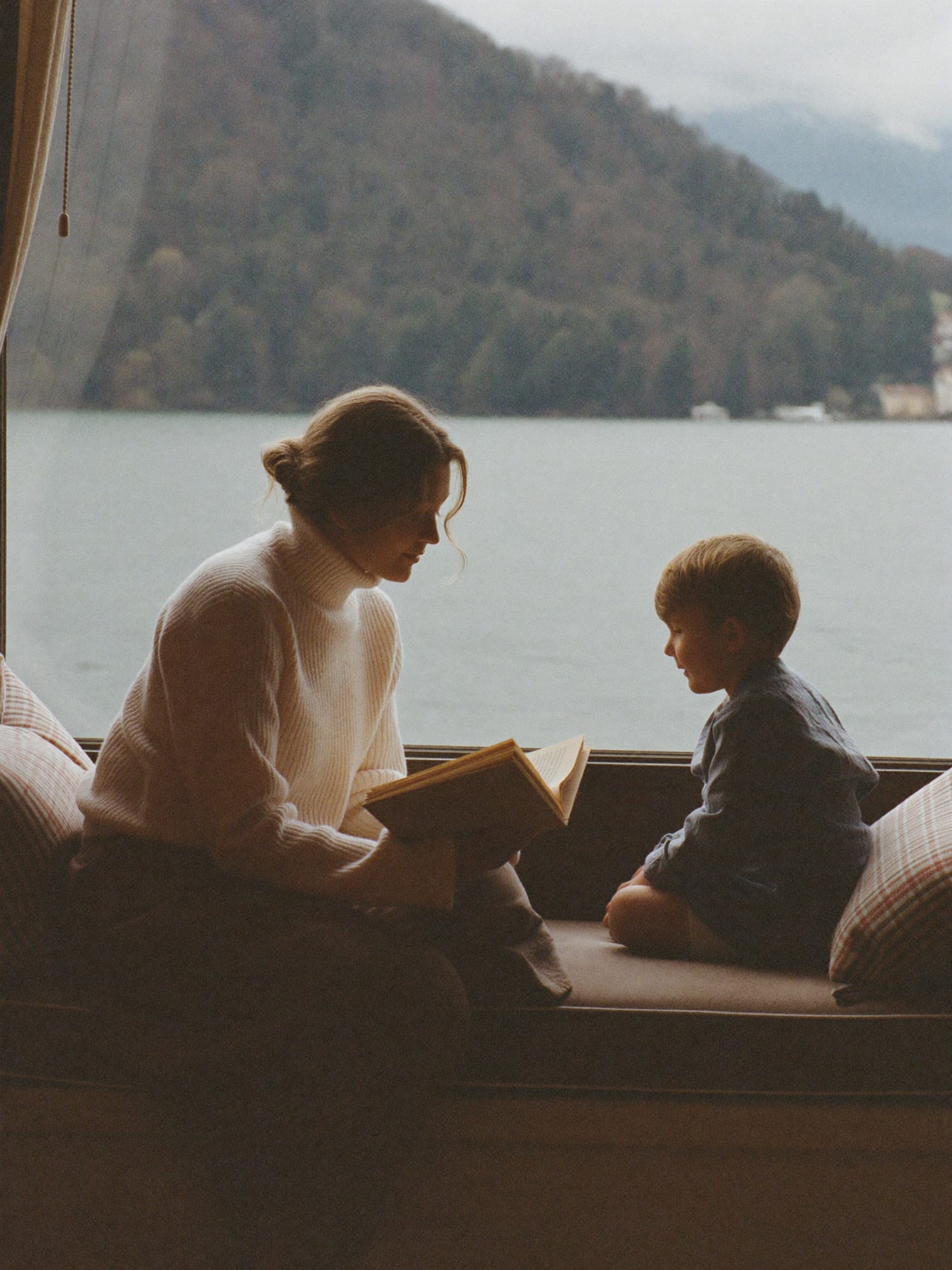 Eine Nanny liest mit einem Kind auf einer Fensterbank ein Bilderbuch