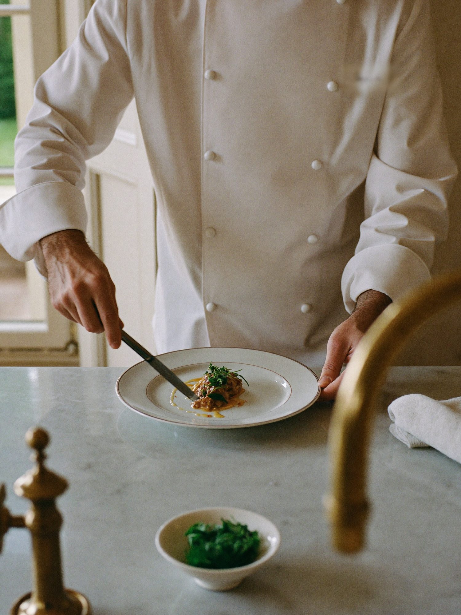 A private chef in a white jacket plating a dish at a marble kitchen island